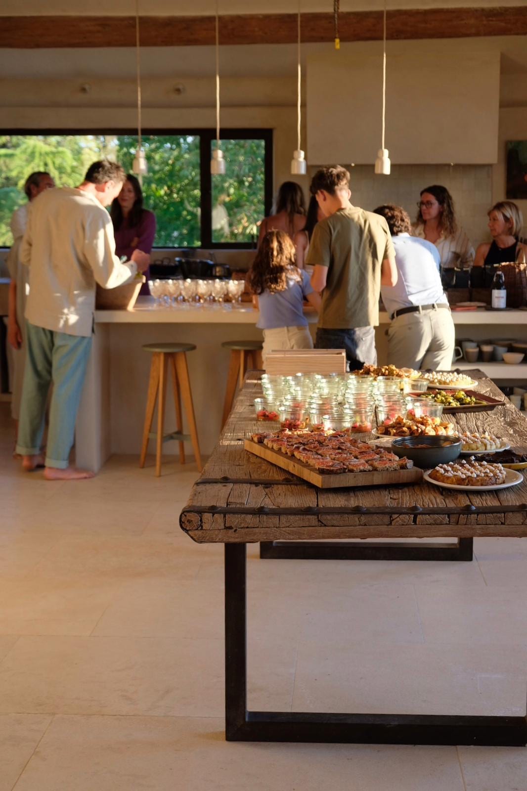 Grande tablée en bois dressée en intérieur, convives autour de l’îlot de cuisine