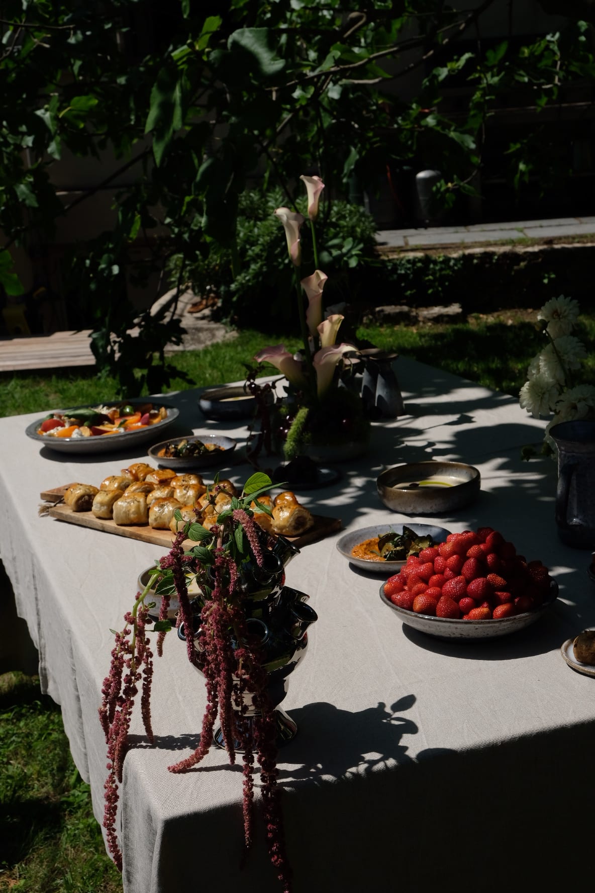 Longue table nappée de lin dressée au jardin, roulés feuilletés, fraises et amarante