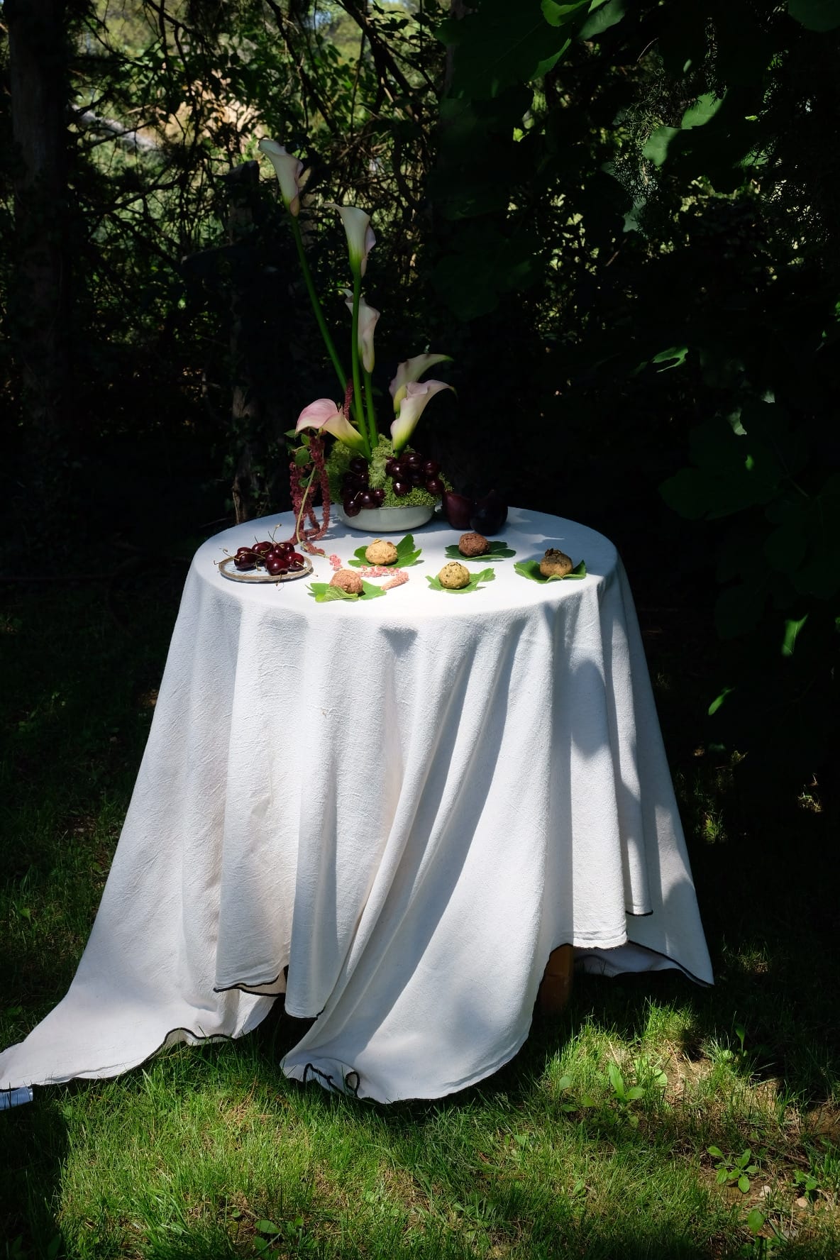 Table ronde nappée de blanc dressée sous les arbres, arums et cerises