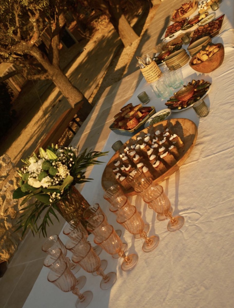 Buffet de tablée sud dressé en extérieur à la lumière rasante du soir, planche de bouchées, verres ambrés et bouquet blanc