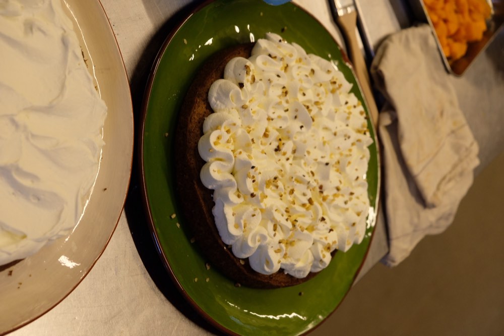 Gâteau nappé de crème fouettée et d'éclats de fruits secs, préparé en cuisine par tablée sud