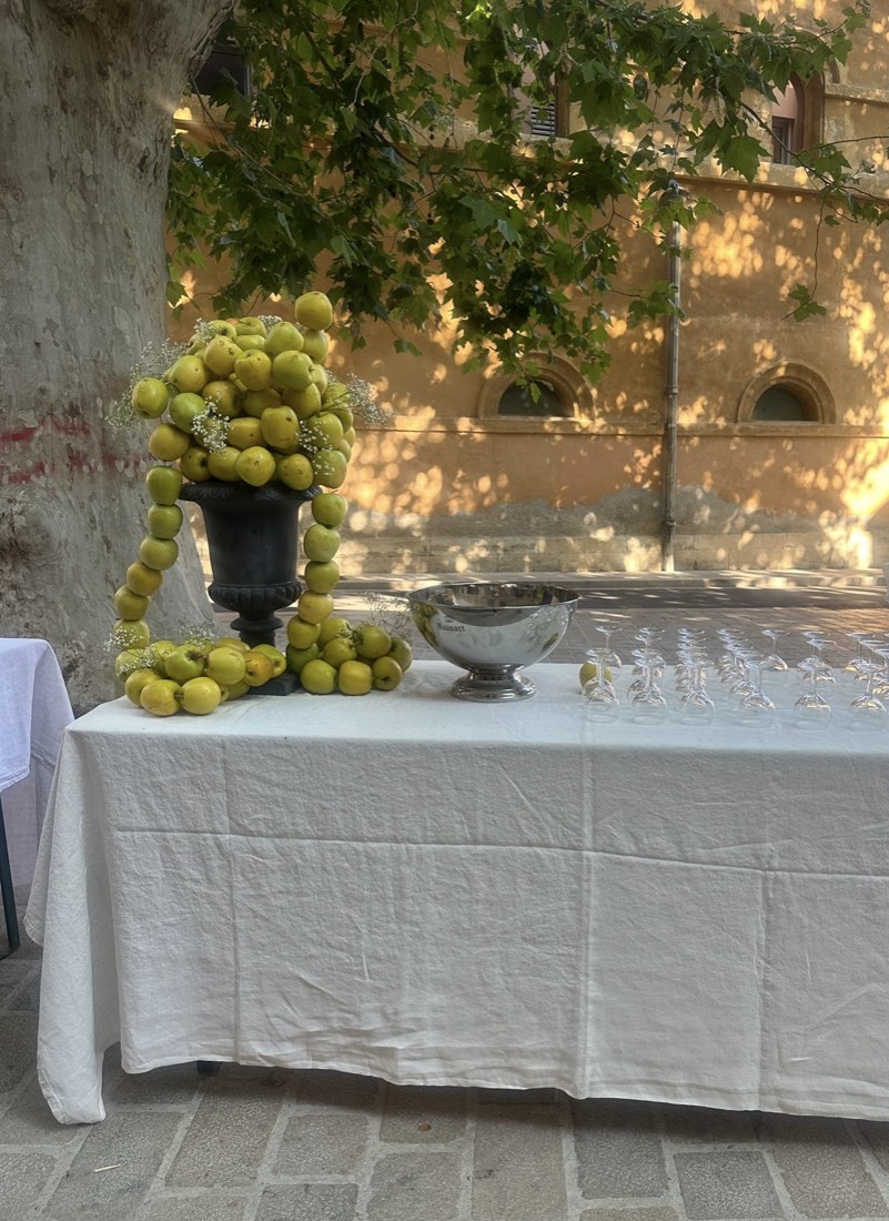 Table d’accueil nappée de lin blanc, verres alignés et composition de pommes vertes
