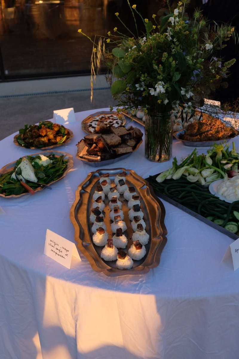 Table ronde dressée au crépuscule par tablée sud : onigiri au maquereau, légumes de saison et bouquet champêtre